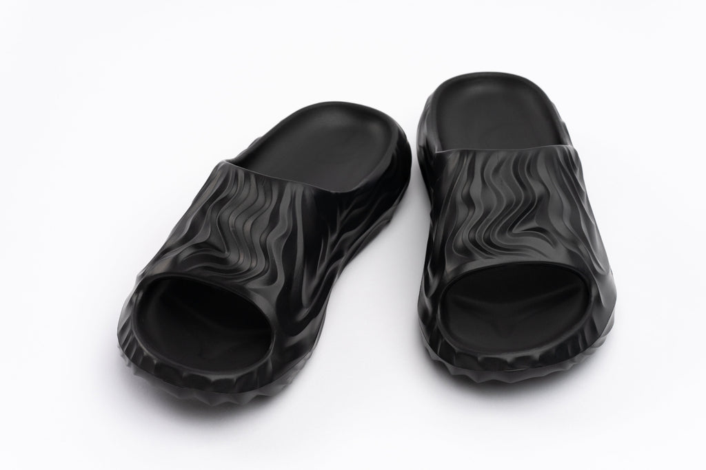 Black slide sandals with wavy pattern on a white background