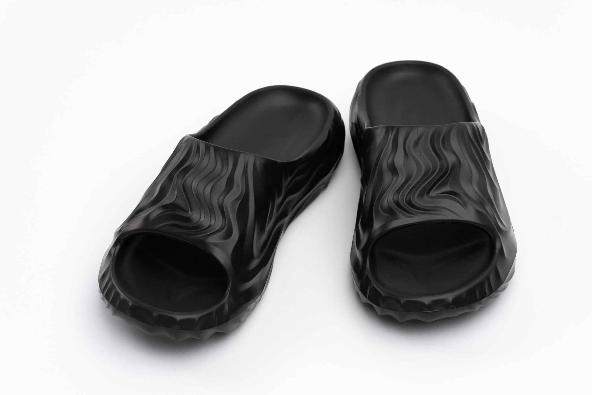 Black slide sandals with wavy pattern on a white background